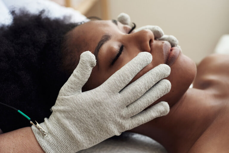 Client receiving a microcurrent facial with conductive gloves to lift and sculpt the face at Spa La La in Austin.