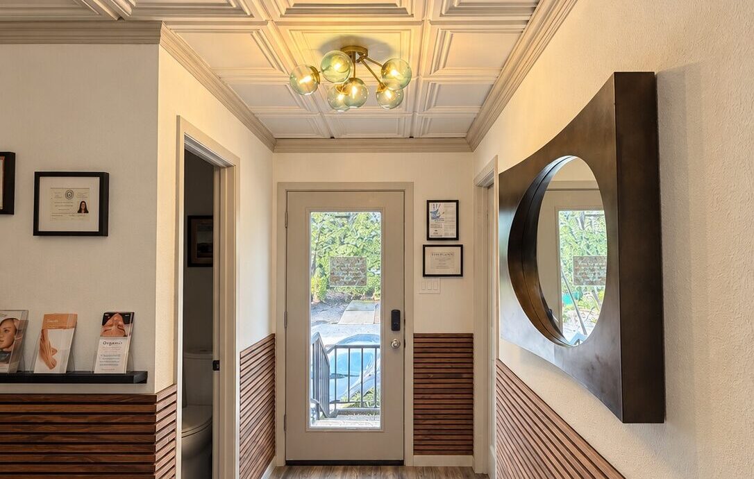 Spa La La entryway in West Lake Hills, Austin, featuring warm wood paneling, a round mirror, and decorative ceiling lighting.